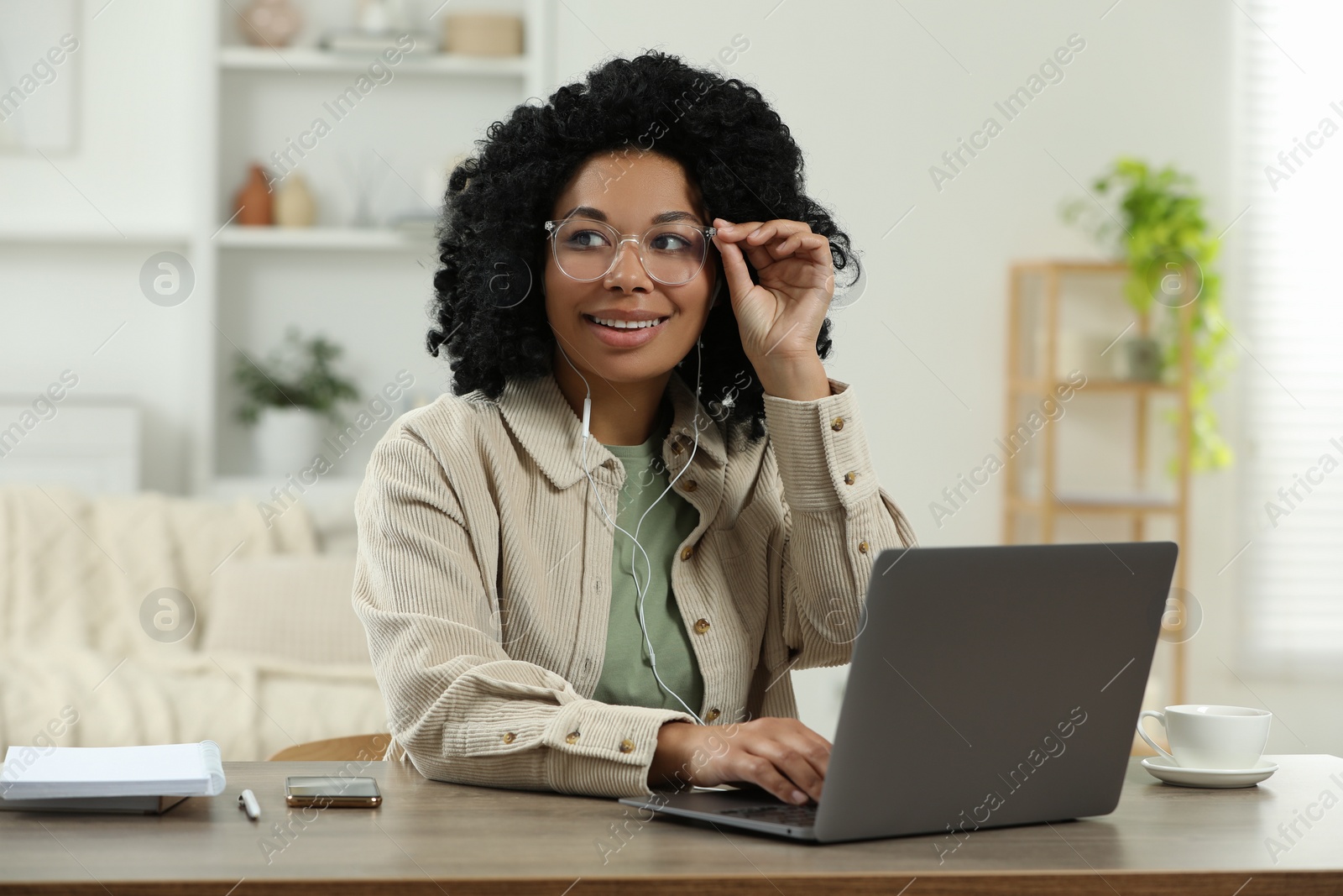 Photo of Happy young woman with laptop at wooden desk indoors