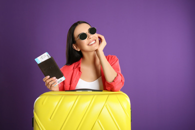 Photo of Beautiful woman with suitcase and ticket in passport for summer trip on purple background. Vacation travel