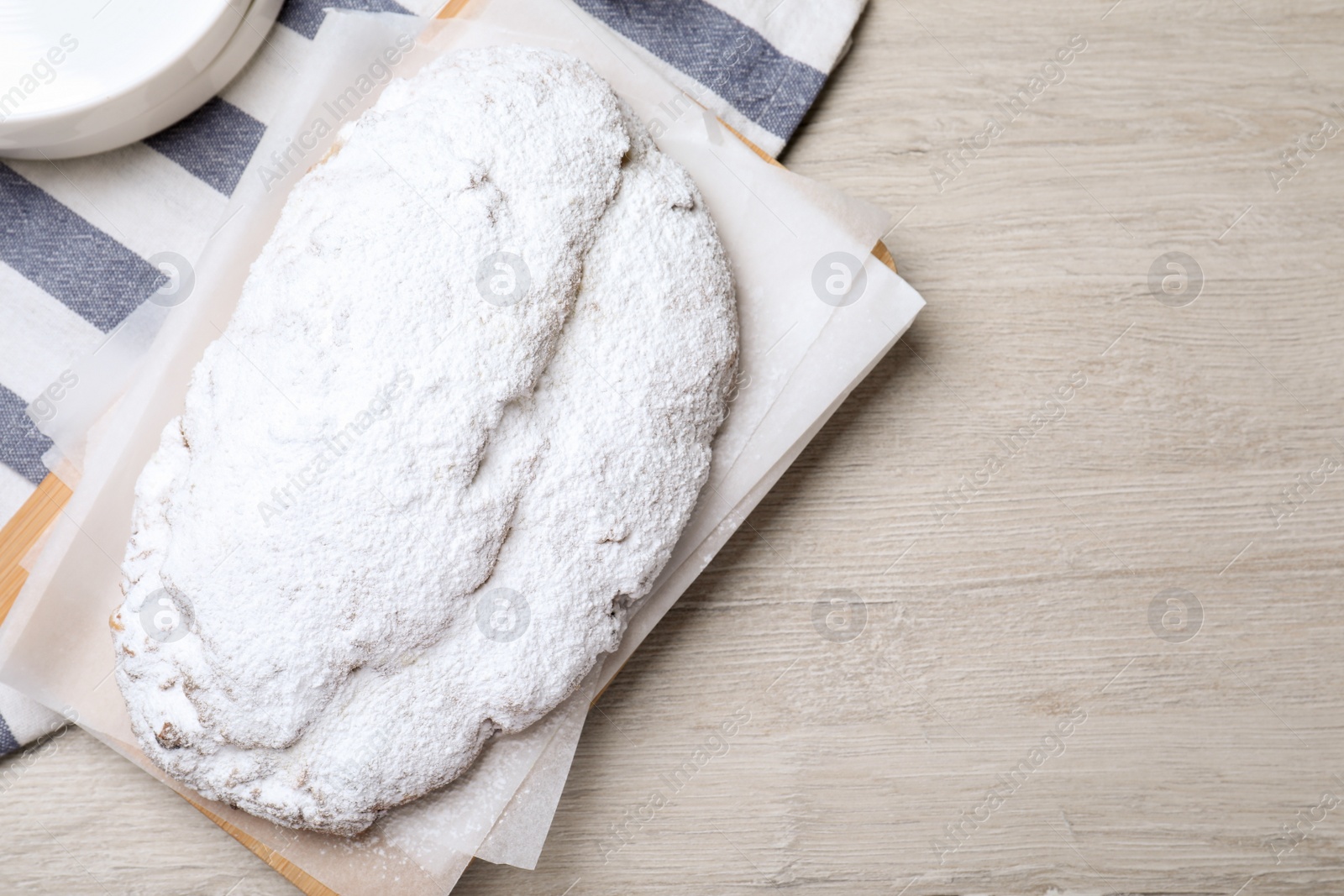 Photo of Delicious Stollen sprinkled with powdered sugar on wooden table, top view. Space for text