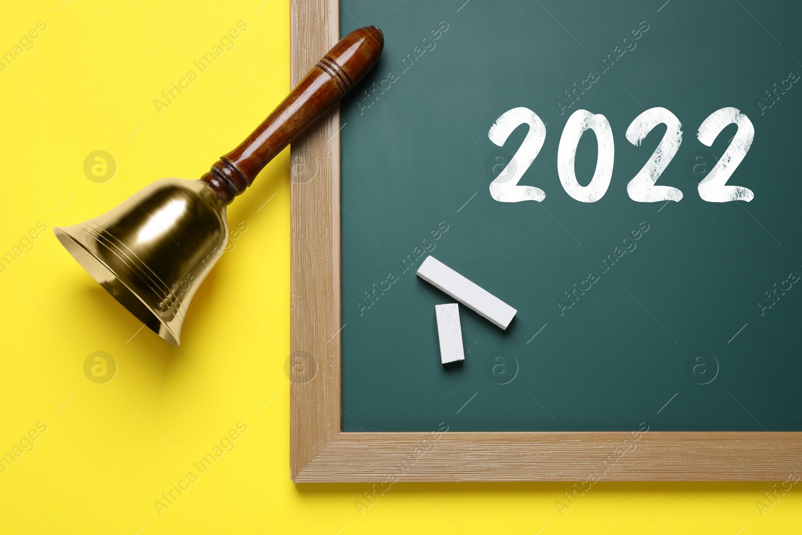 Image of Back to school 2022. Golden bell, green board and pieces of chalk on yellow background, flat lay