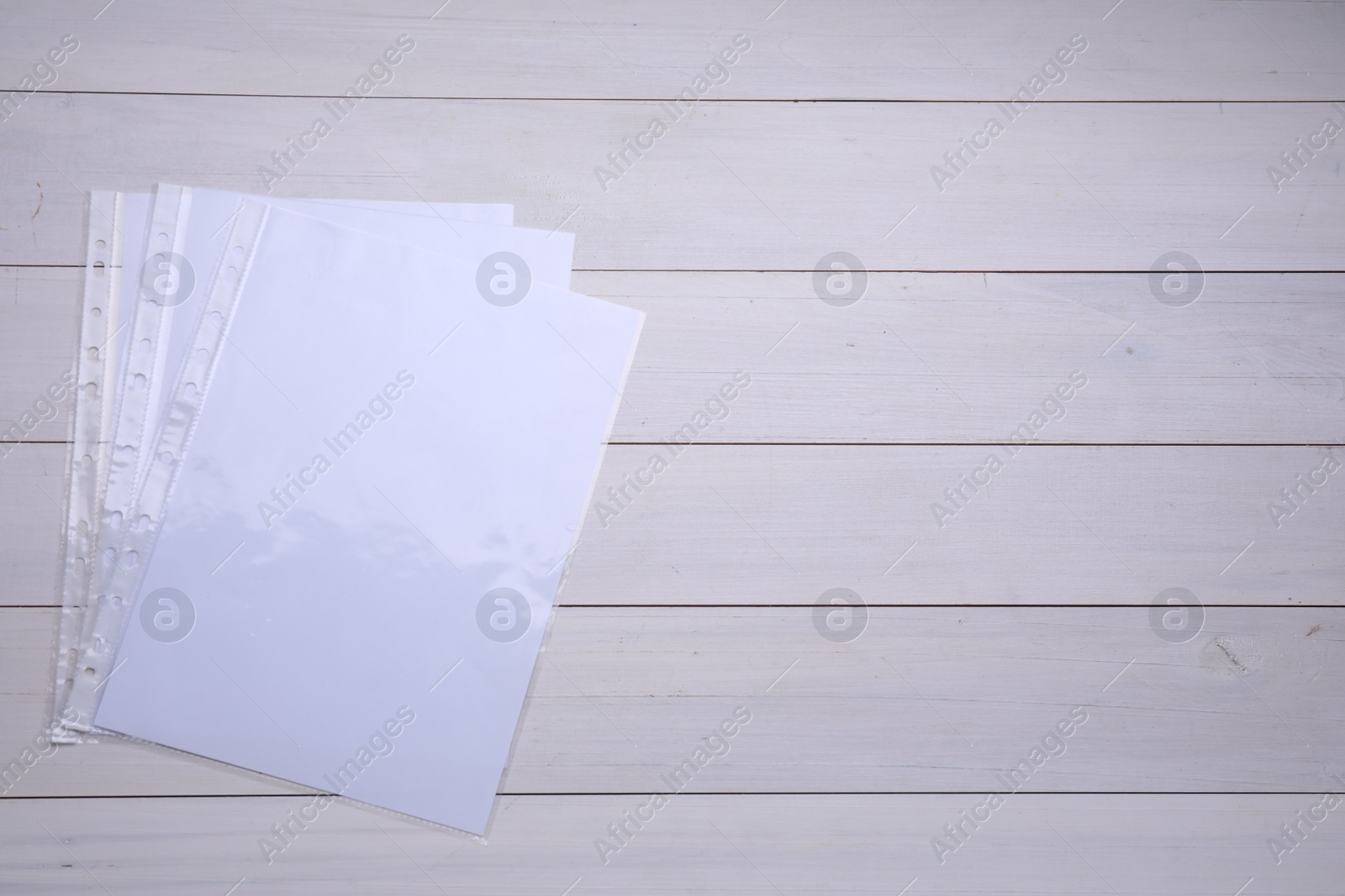 Photo of Punched pockets with paper sheets on white wooden table, flat lay. Space for text