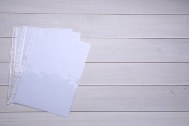 Photo of Punched pockets with paper sheets on white wooden table, flat lay. Space for text