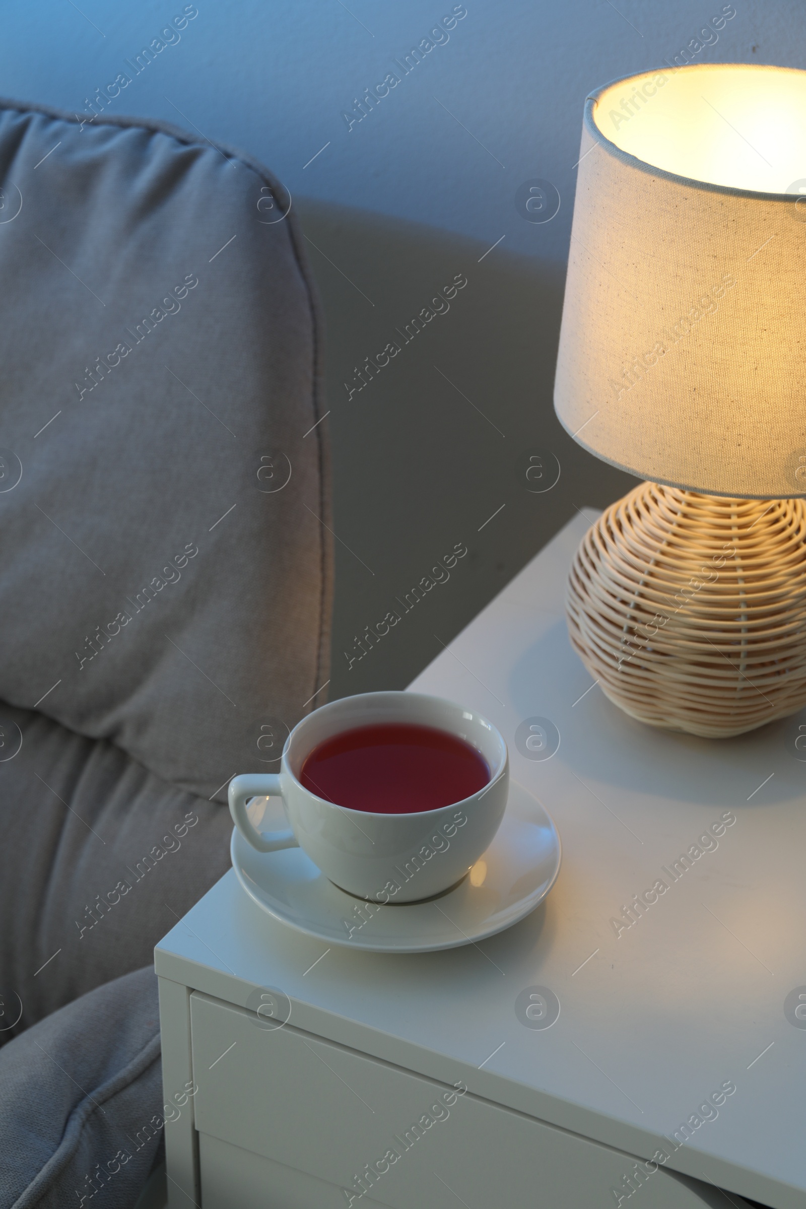 Photo of Cup of hot tea and nightlight on white table at night