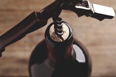 Opening wine bottle with corkscrew on blurred background, closeup