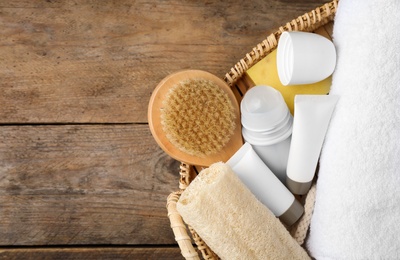 Photo of Natural deodorant and bath accessories in basket on wooden table, flat lay