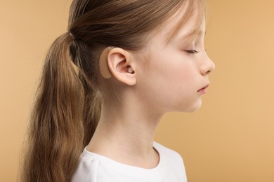 Little girl with hearing aid on pale brown background, closeup