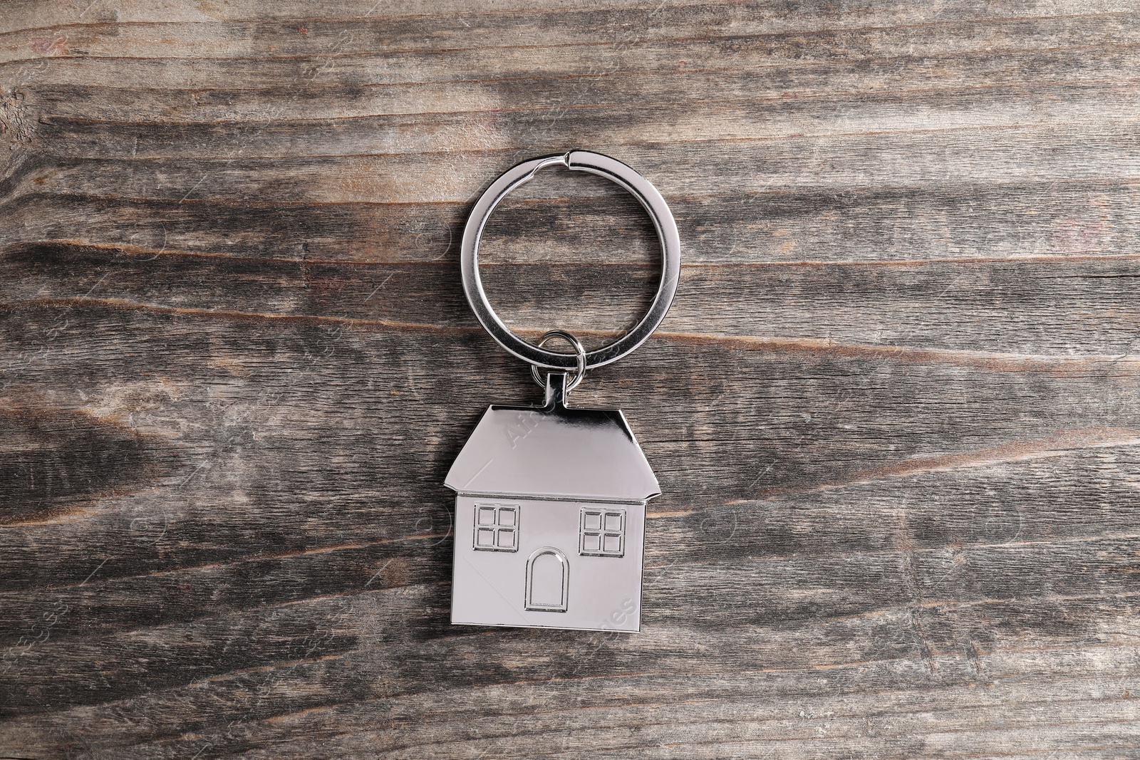 Photo of Metal keychain in shape of house on rustic wooden table, top view