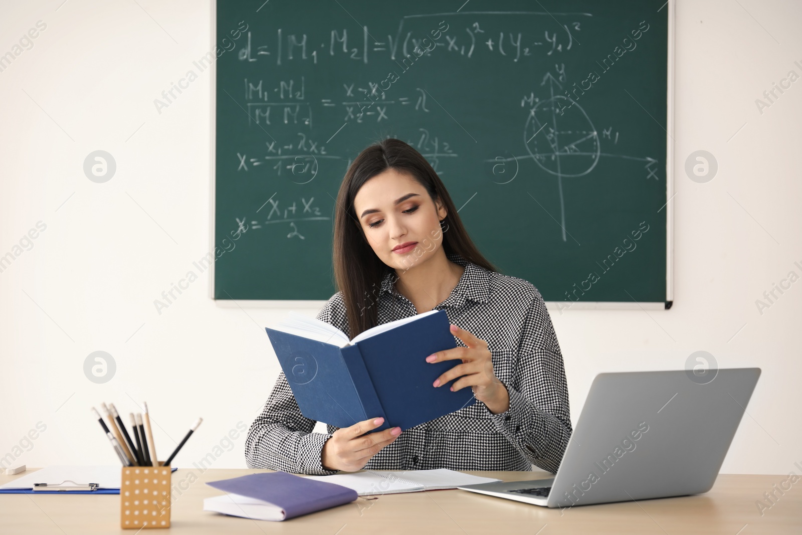 Photo of Young female teacher working at table in classroom