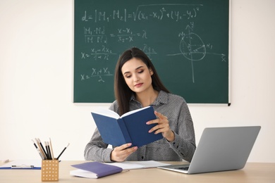 Young female teacher working at table in classroom