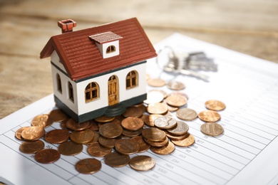 Photo of House model with coins and document on table, closeup. Real estate agent service