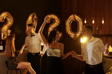 Photo of Young people celebrating New Year in club. Golden 2020 balloons on background