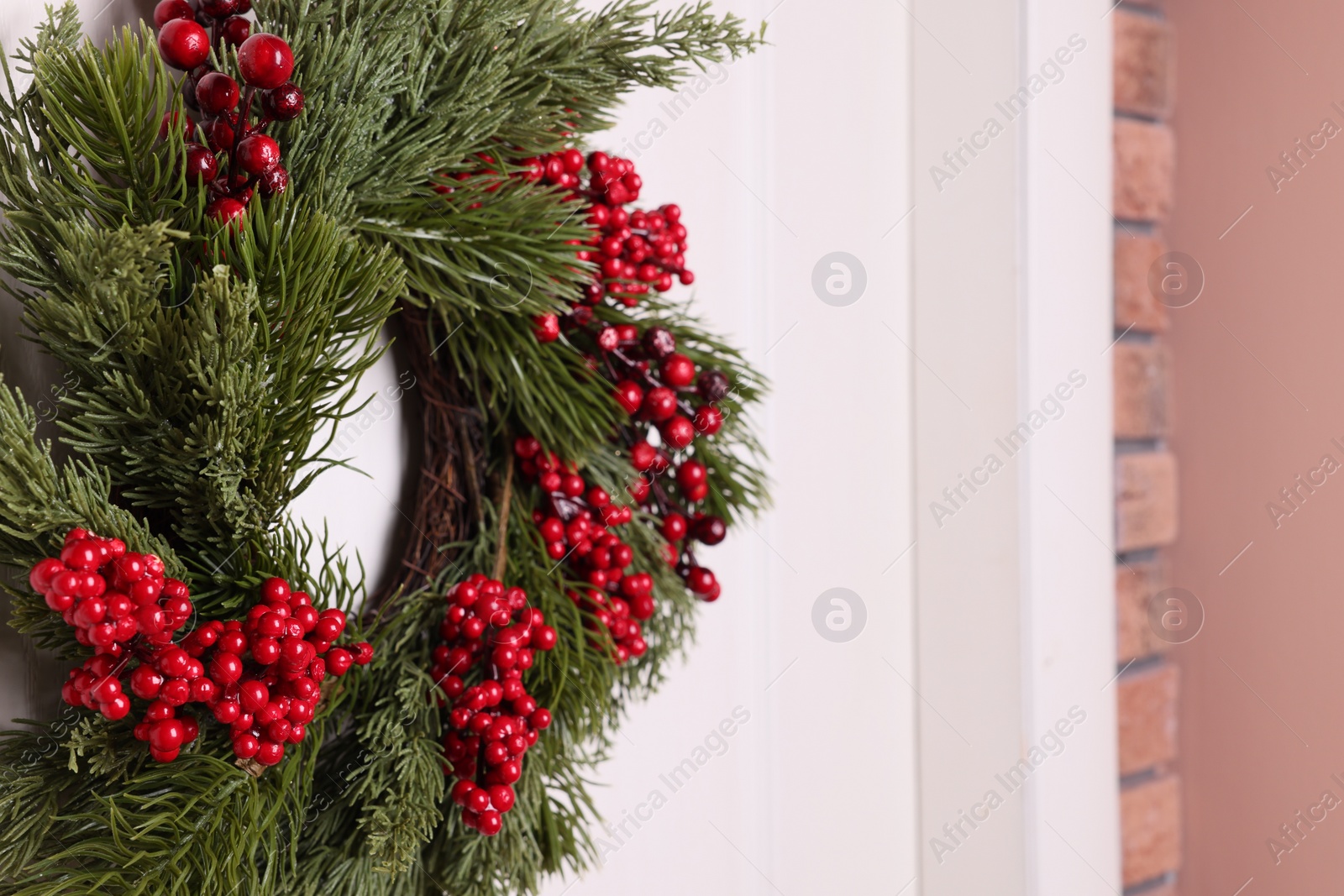 Photo of Beautiful Christmas wreath with red berries hanging on white door, closeup. Space for text