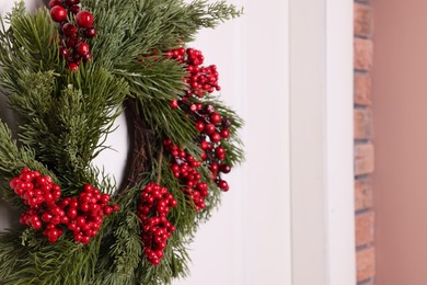 Beautiful Christmas wreath with red berries hanging on white door, closeup. Space for text