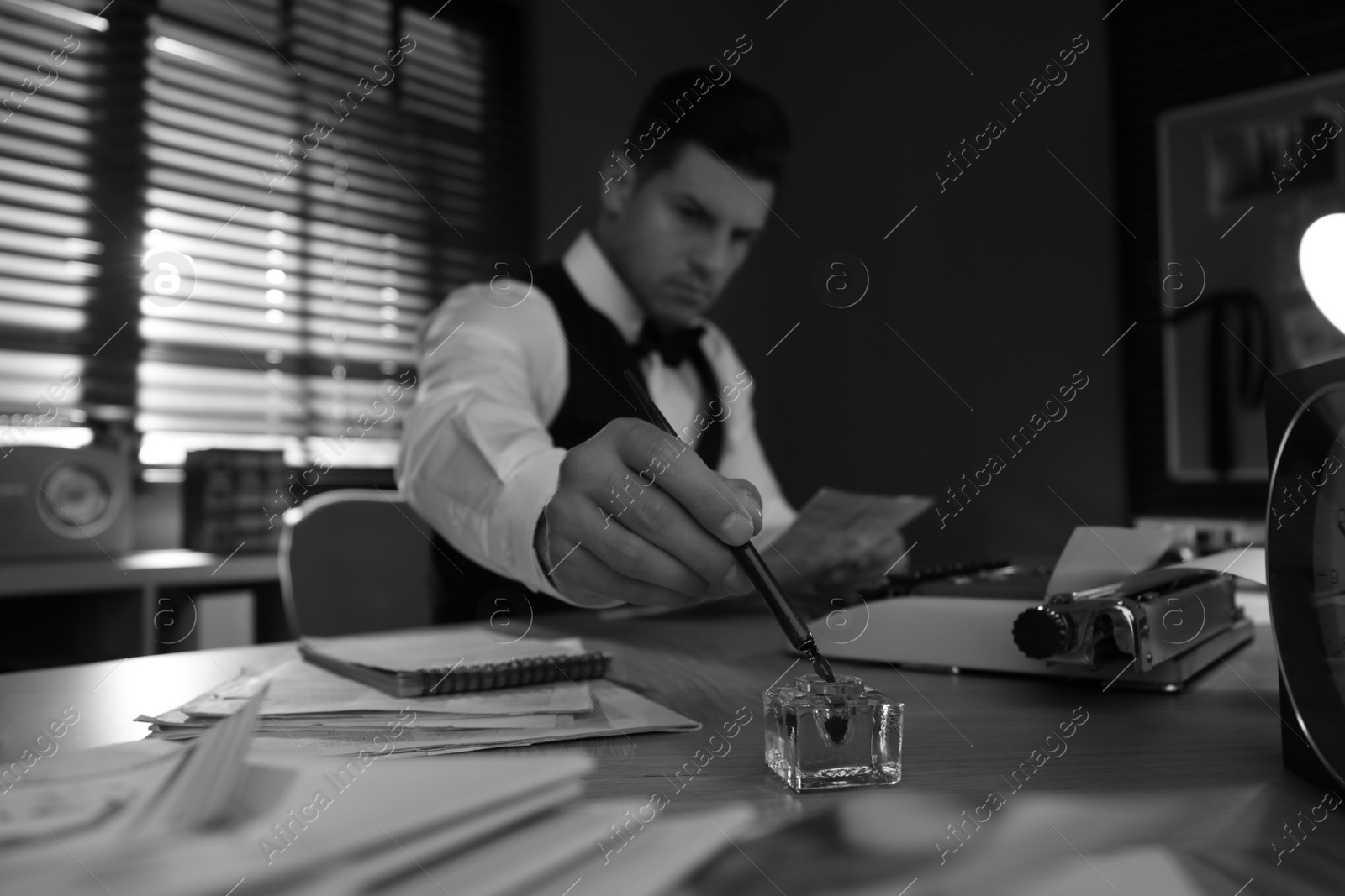 Photo of Old fashioned detective working at table in office, focus on hand with ink pen. Black and white effect
