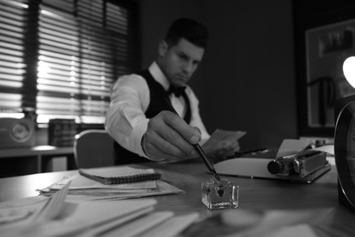 Old fashioned detective working at table in office, focus on hand with ink pen. Black and white effect