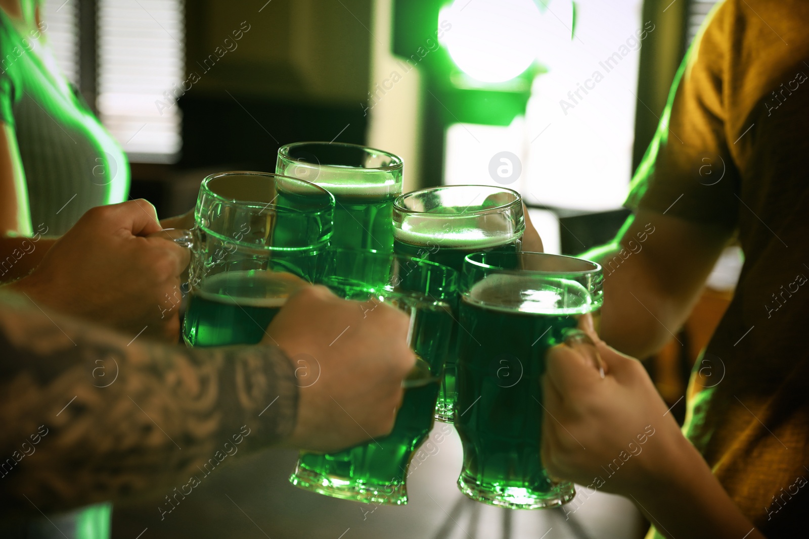 Photo of Group of friends toasting with green beer in pub, closeup. St. Patrick's Day celebration