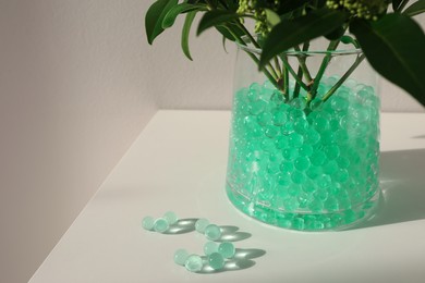 Photo of Mint filler and green branches in glass vase on white table, space for text. Water beads
