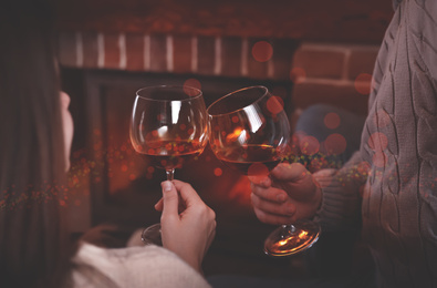 Lovely couple with glasses of wine resting near fireplace at home, closeup. Winter vacation