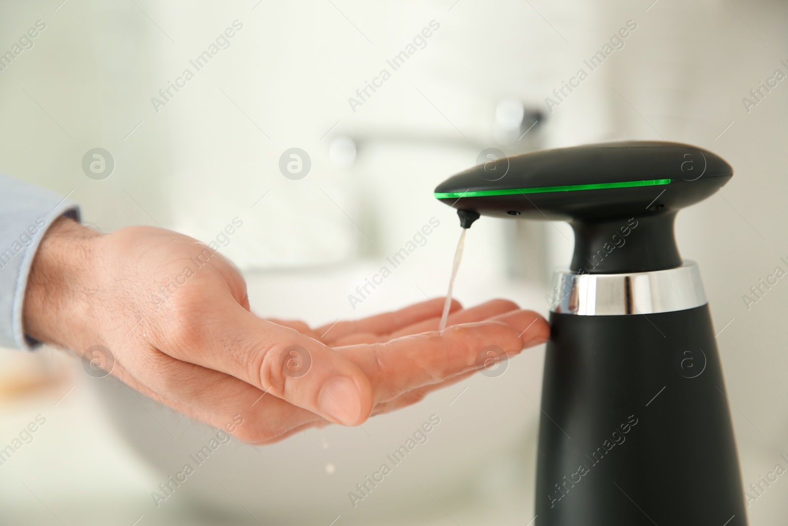 Photo of Man using automatic soap dispenser in bathroom, closeup