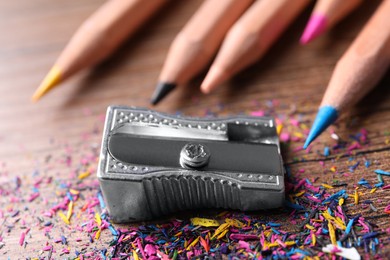 Photo of Metal sharpener, colorful graphite crumbs and pencils on brown wooden table, closeup