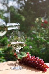 Photo of Pouring white wine from bottle into glass at wooden table outdoors, closeup. Space for text