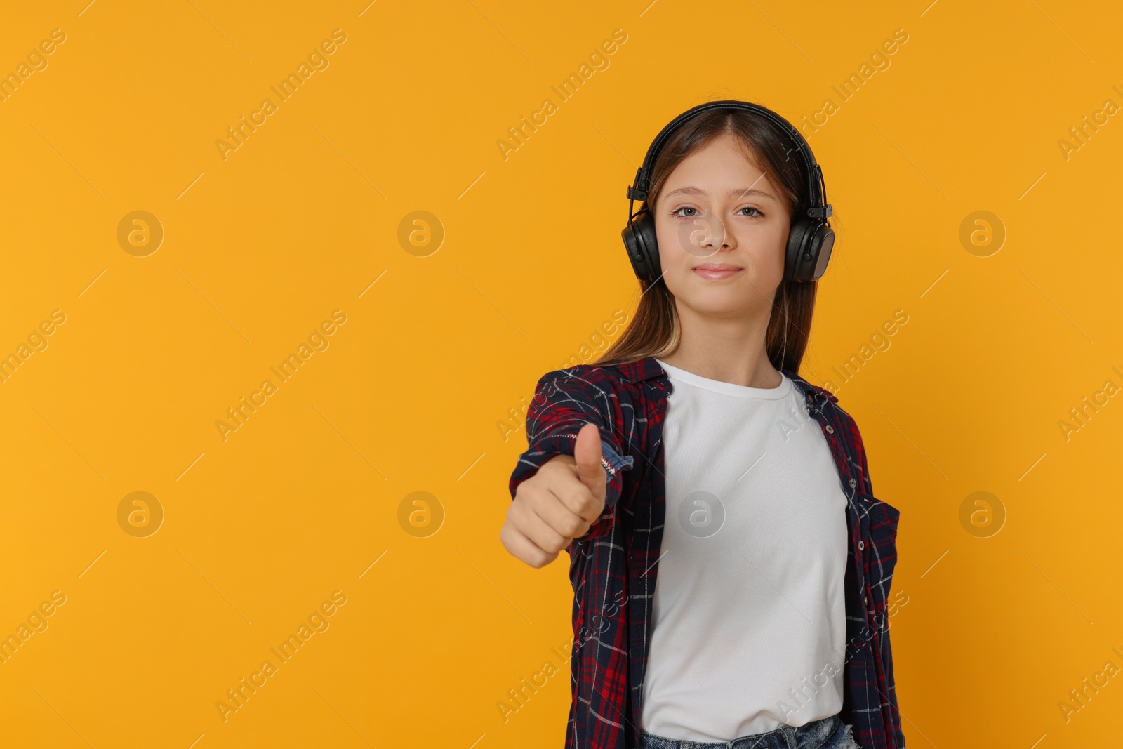 Photo of Teenage girl listening to music with headphones on orange background. Space for text
