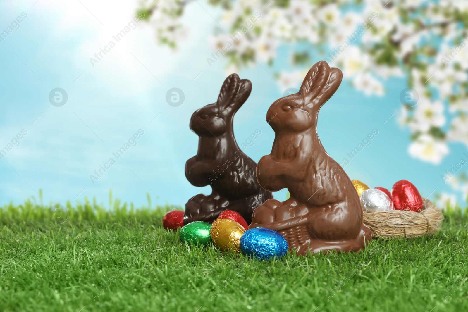 Image of Chocolate bunnies and eggs on green grass outdoors, space for text.. Easter celebration