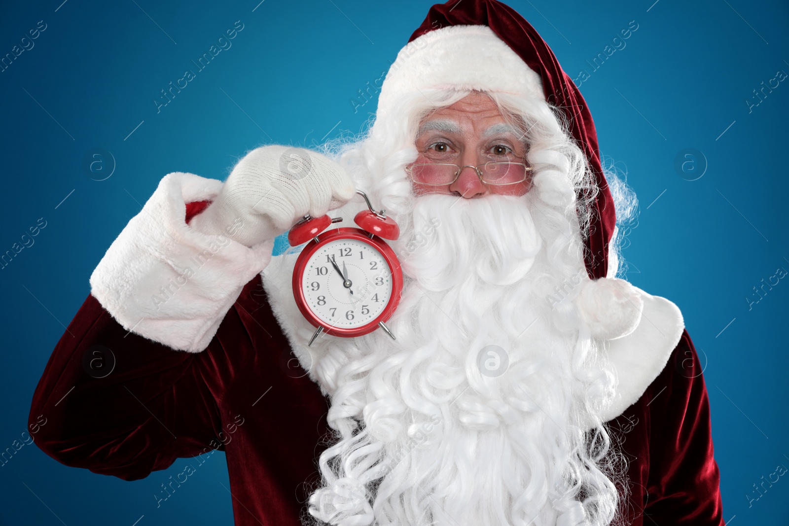 Photo of Santa Claus holding alarm clock on blue background. Christmas countdown