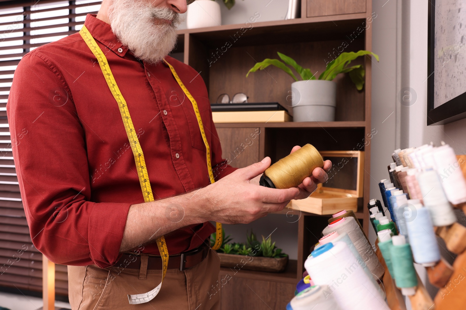 Photo of Professional tailor choosing thread near stand in workshop, closeup