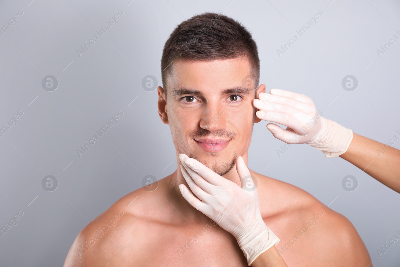 Photo of Doctor examining man's face for cosmetic surgery on grey background