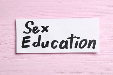 Photo of Piece of paper with phrase "SEX EDUCATION" on pink wooden background, top view