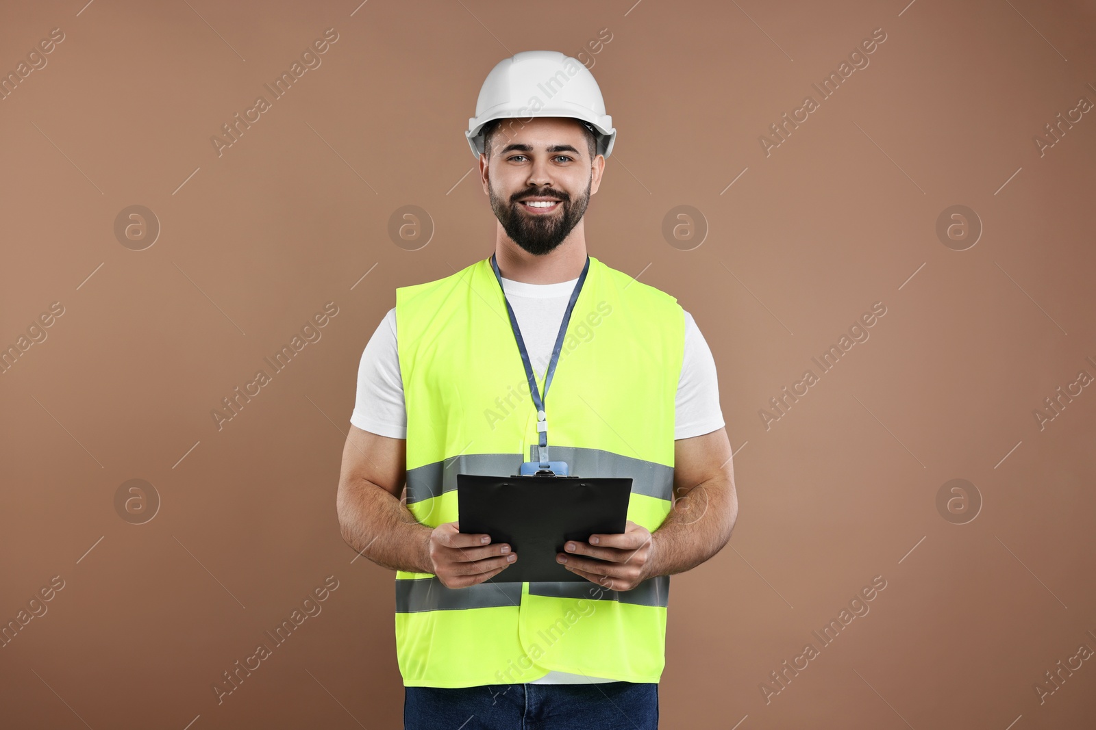 Photo of Engineer in hard hat holding clipboard on brown background