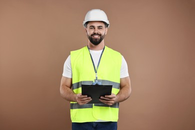 Engineer in hard hat holding clipboard on brown background