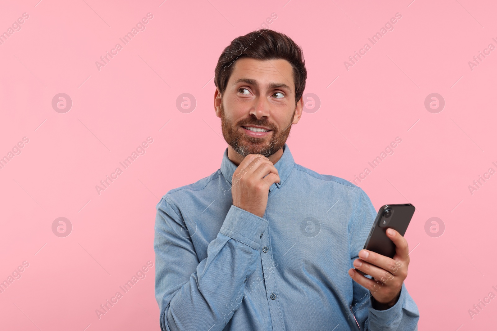 Photo of Handsome bearded man using smartphone on pink background