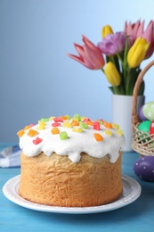 Easter cake, colorful eggs and tulips on light blue table
