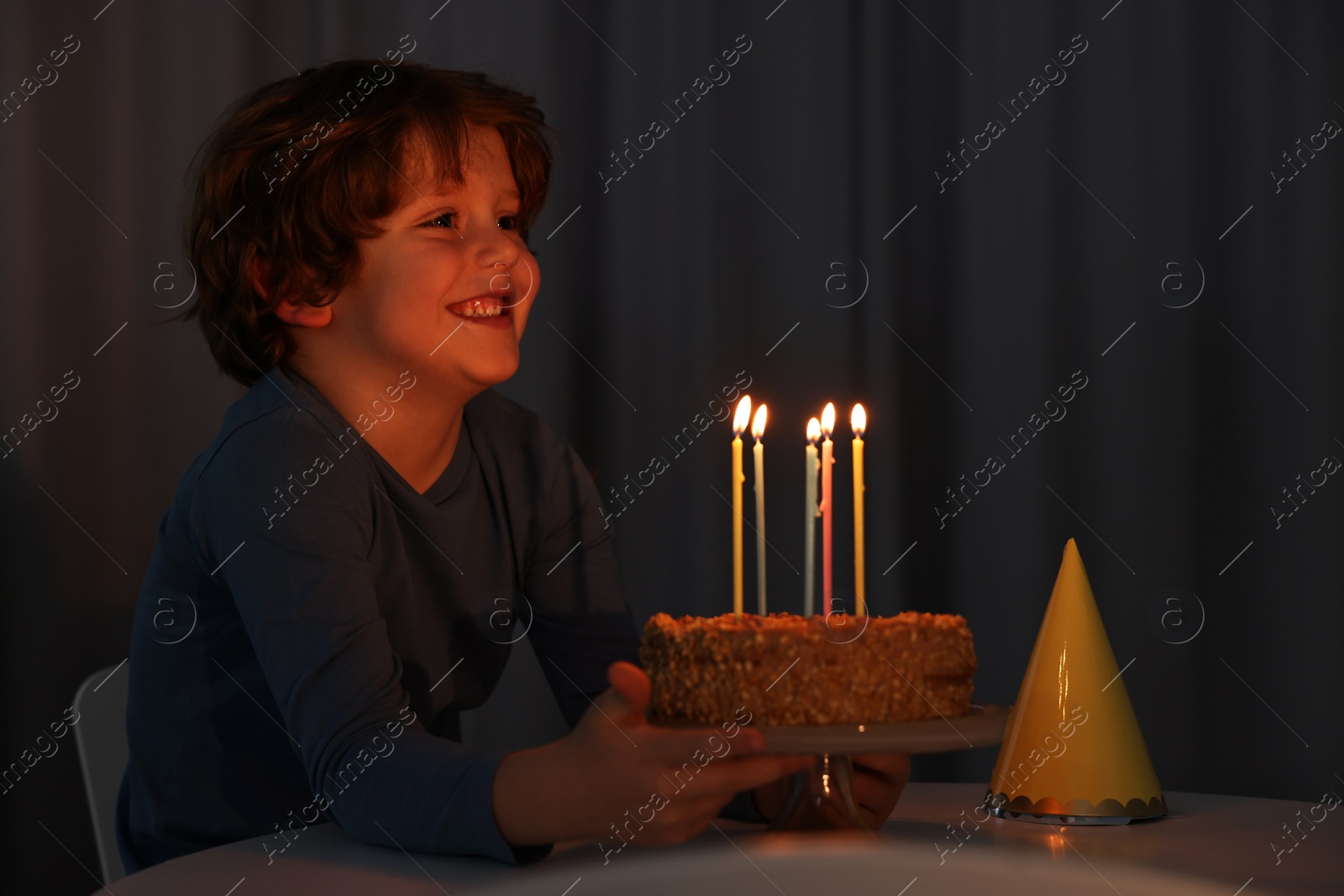 Photo of Cute boy with birthday cake at table indoors