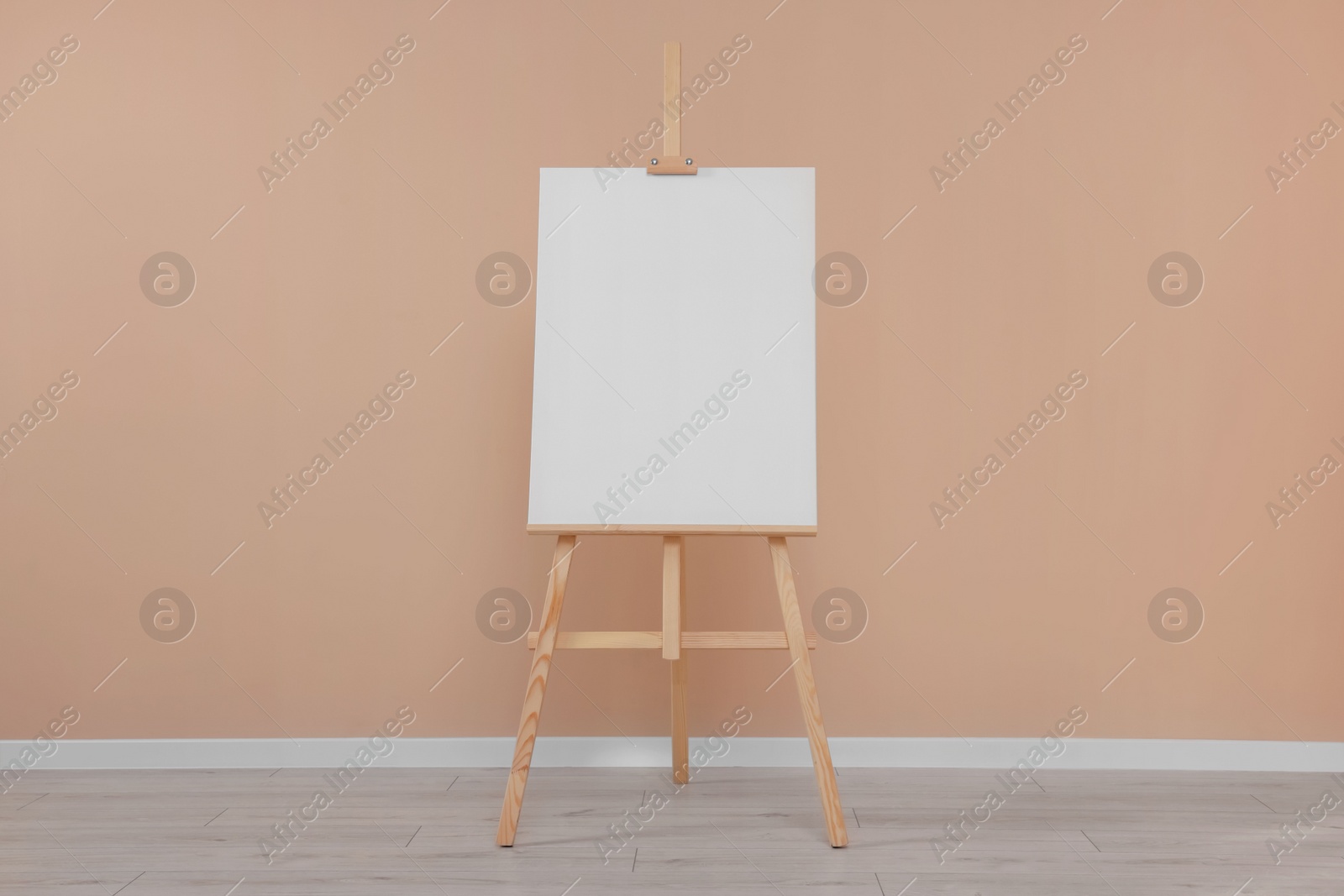 Photo of Wooden easel with blank canvas near beige wall indoors.