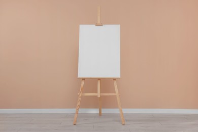 Photo of Wooden easel with blank canvas near beige wall indoors.