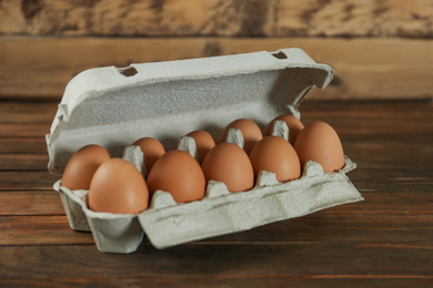 Raw chicken eggs in carton on wooden table