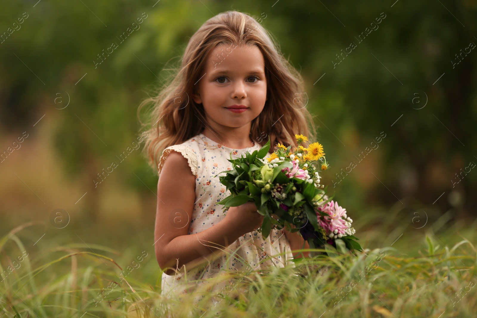 Photo of Cute little girl holding wreath made of beautiful flowers in field