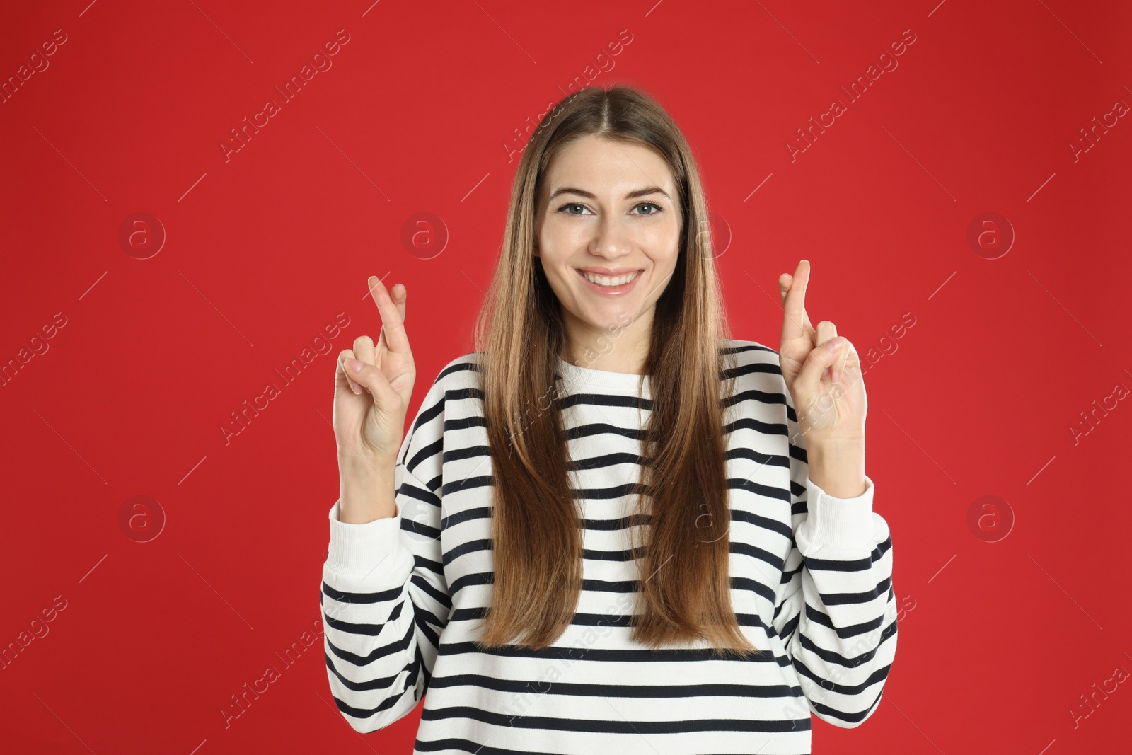 Photo of Woman with crossed fingers on red background. Superstition concept