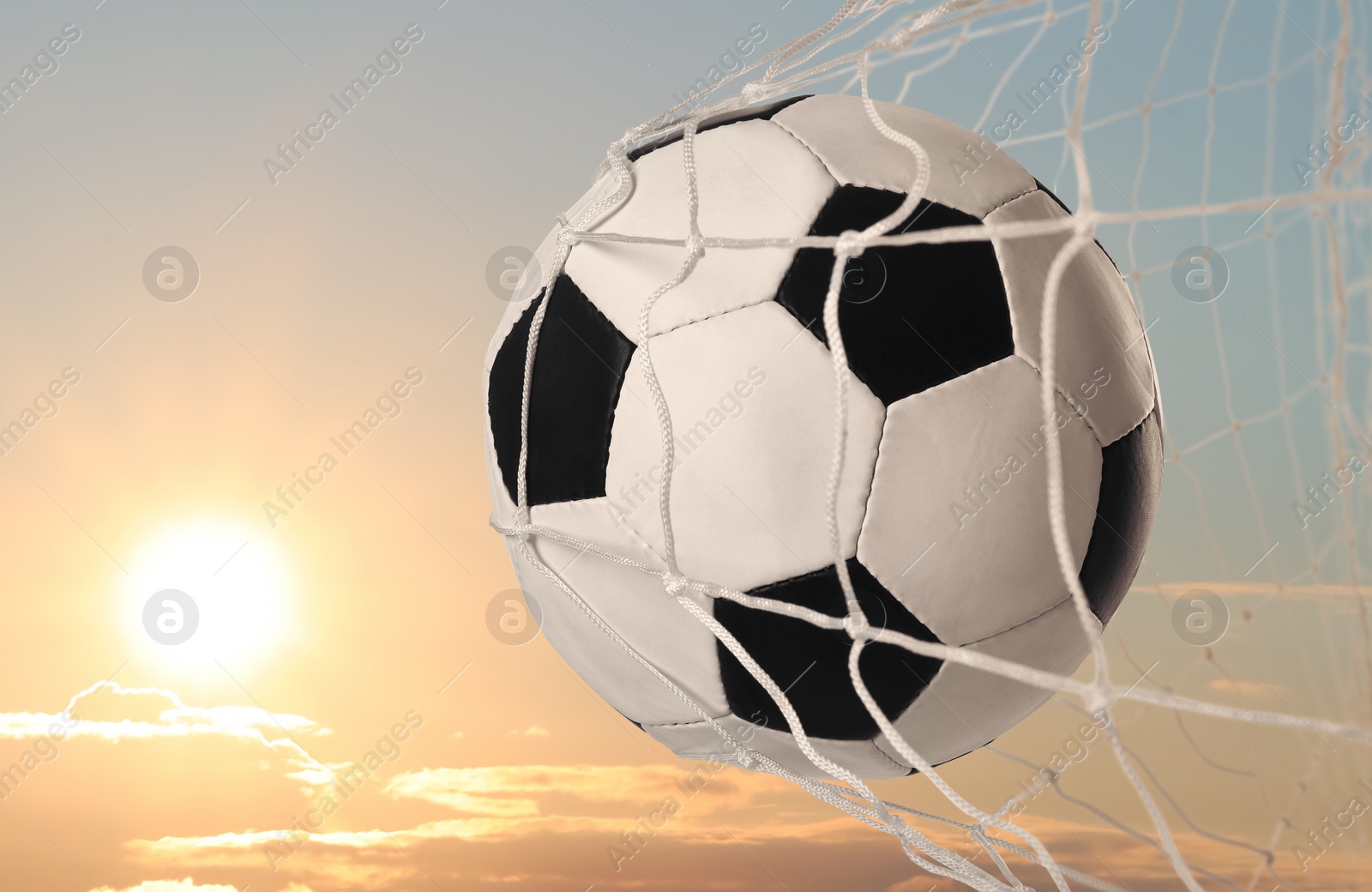 Image of Soccer ball in net against sky at sunset