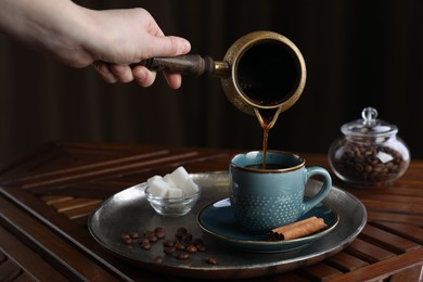 Photo of Turkish coffee. Woman pouring brewed beverage from cezve into cup at wooden table, closeup