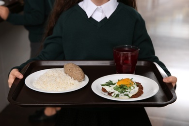 Photo of Girl holding tray with healthy food in school canteen, closeup