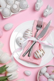 Photo of Festive table setting with painted eggs and tulips on pink background, above view. Easter celebration