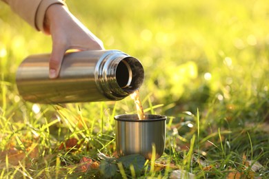 Photo of Woman pouring tea from thermos into cup lid on green grass outdoors, closeup. Space for text