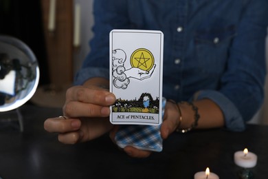 Photo of Fortune teller with tarot card Ace of Pentacles at grey table indoors, closeup