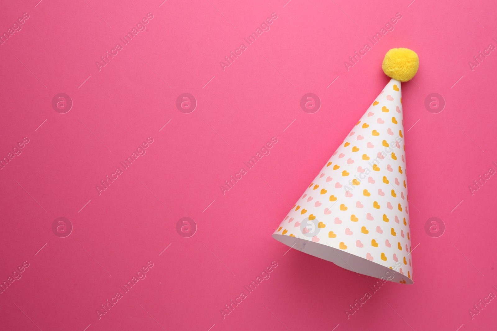 Photo of One party hat with hearts on pink background, top view. Space for text
