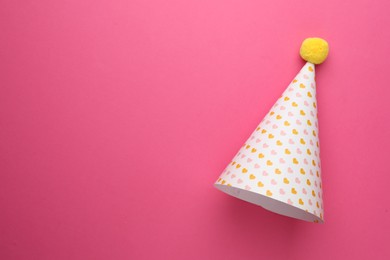 One party hat with hearts on pink background, top view. Space for text