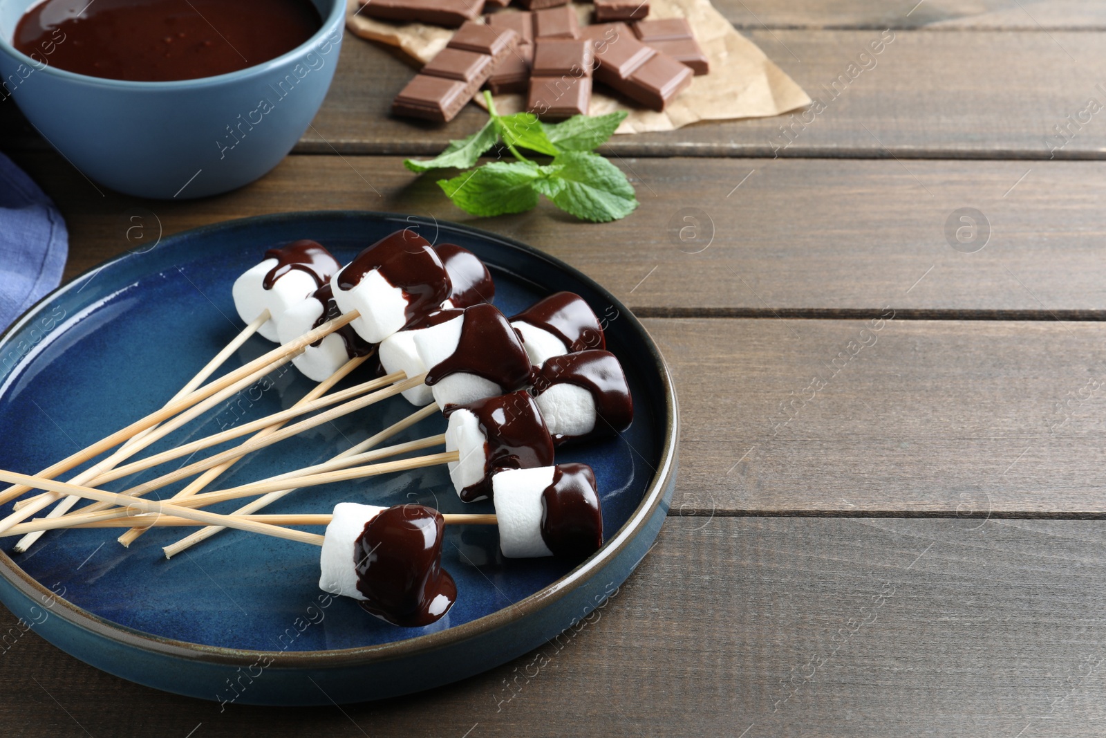 Photo of Delicious marshmallows covered with chocolate on wooden table, space for text